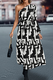 Black and white geometric print asymmetric maxi dress with belt and one long sleeve.