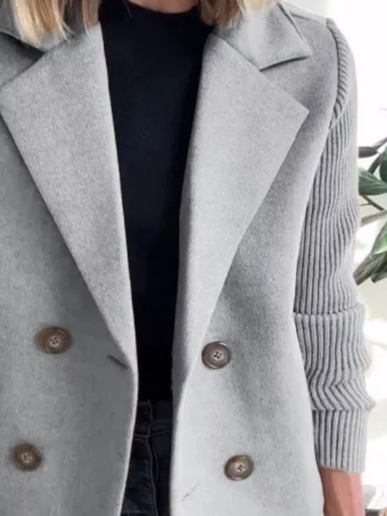 Light gray double-breasted trench coat with knit sleeves and brown buttons.