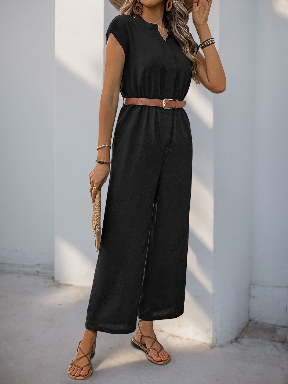 Black cap-sleeve wide-leg jumpsuit with a V-neck and belted waist, styled with sandals.