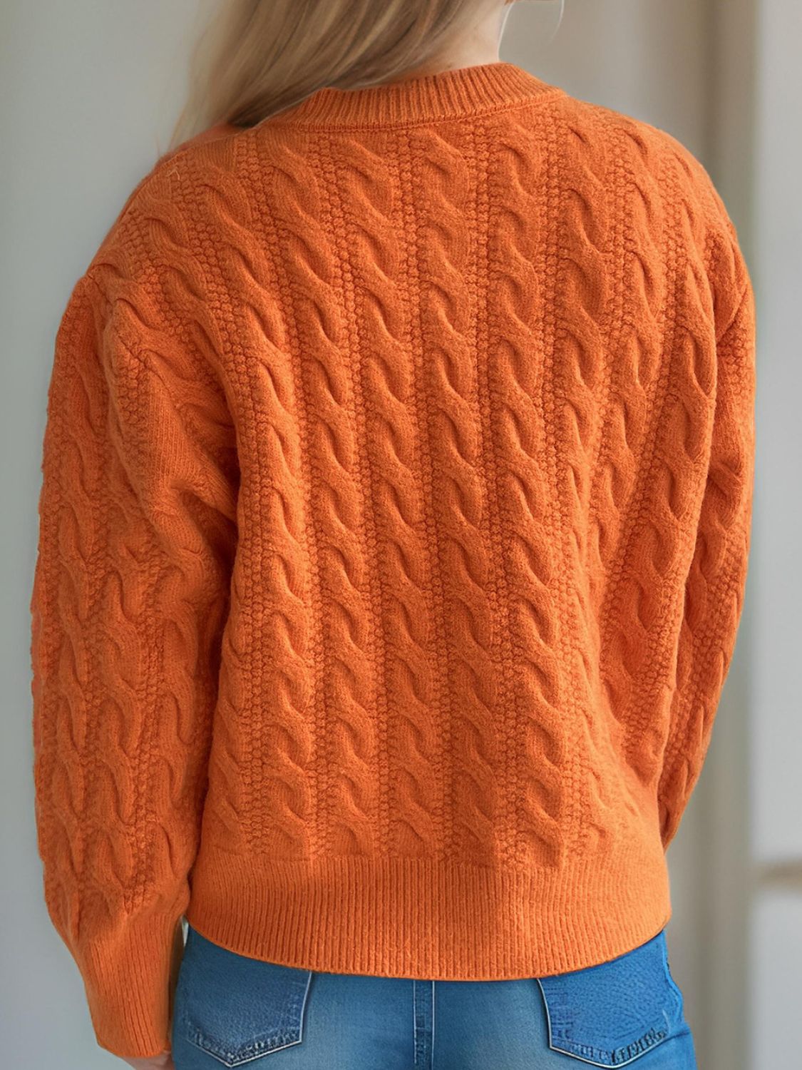Orange cable knit cardigan with puff sleeves and buttoned front.