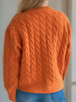 Orange cable knit cardigan with puff sleeves and buttoned front.