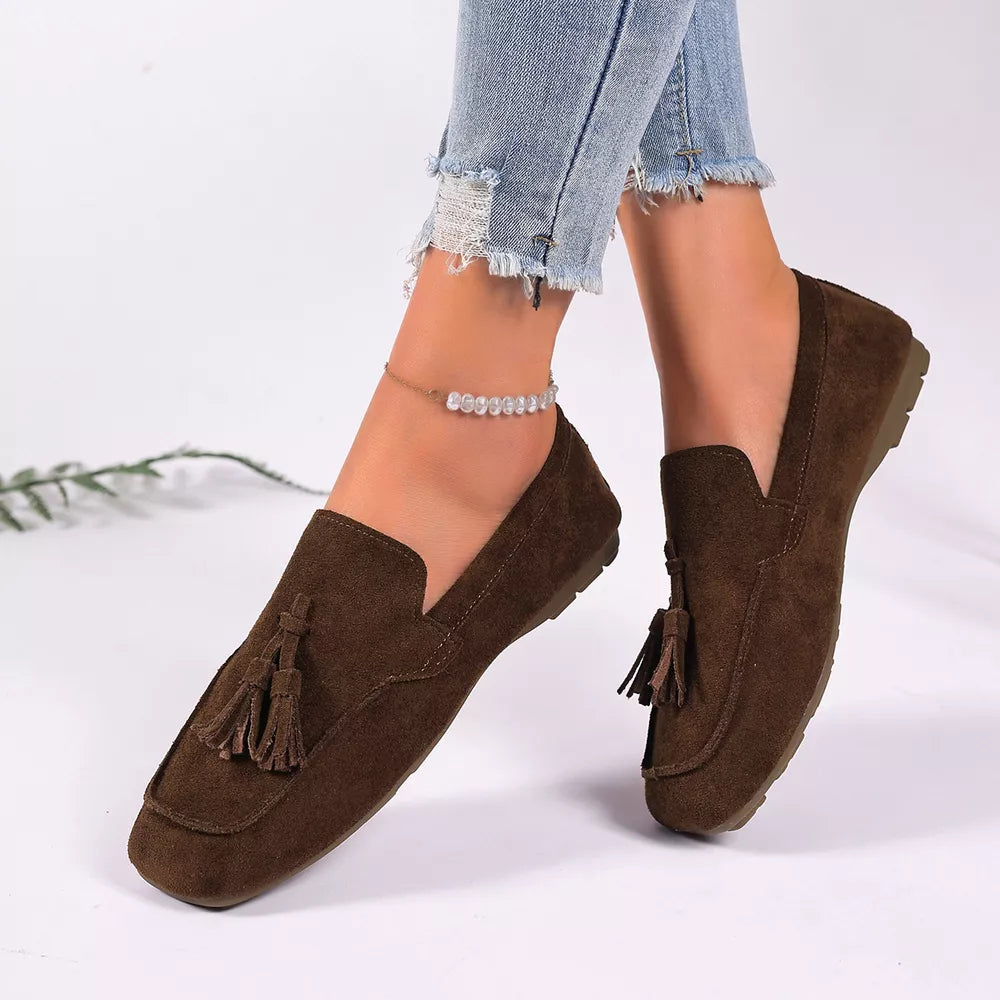 Brown suede slip-on loafers with tassel embellishments and a square toe.
