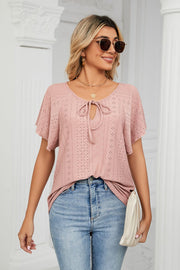Pink eyelet tie-neck blouse with flutter sleeves and a V-neck.