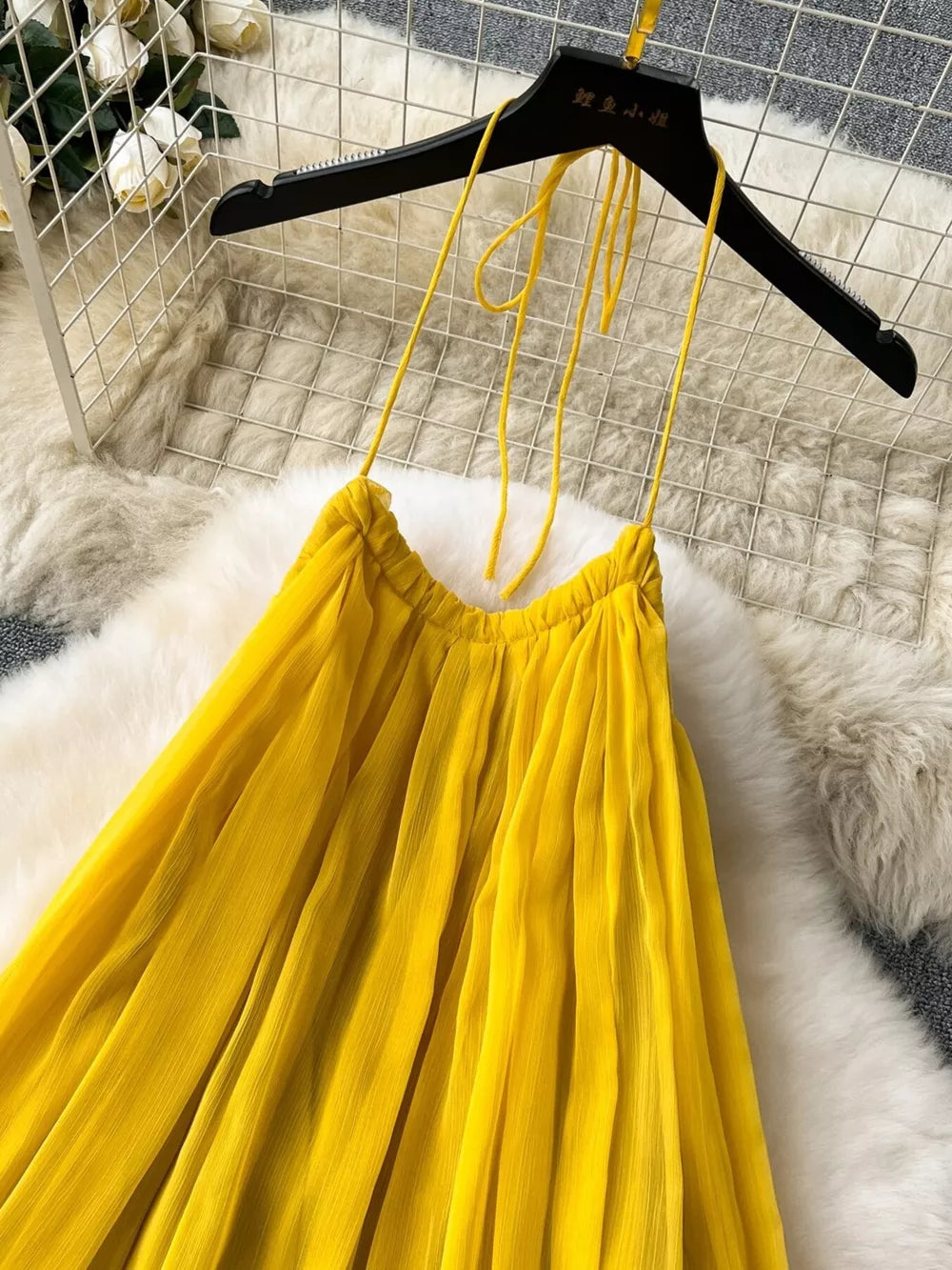 Yellow chiffon halter dress with tie straps and pleated skirt detail.