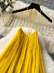 Yellow chiffon halter dress with tie straps and pleated skirt detail.