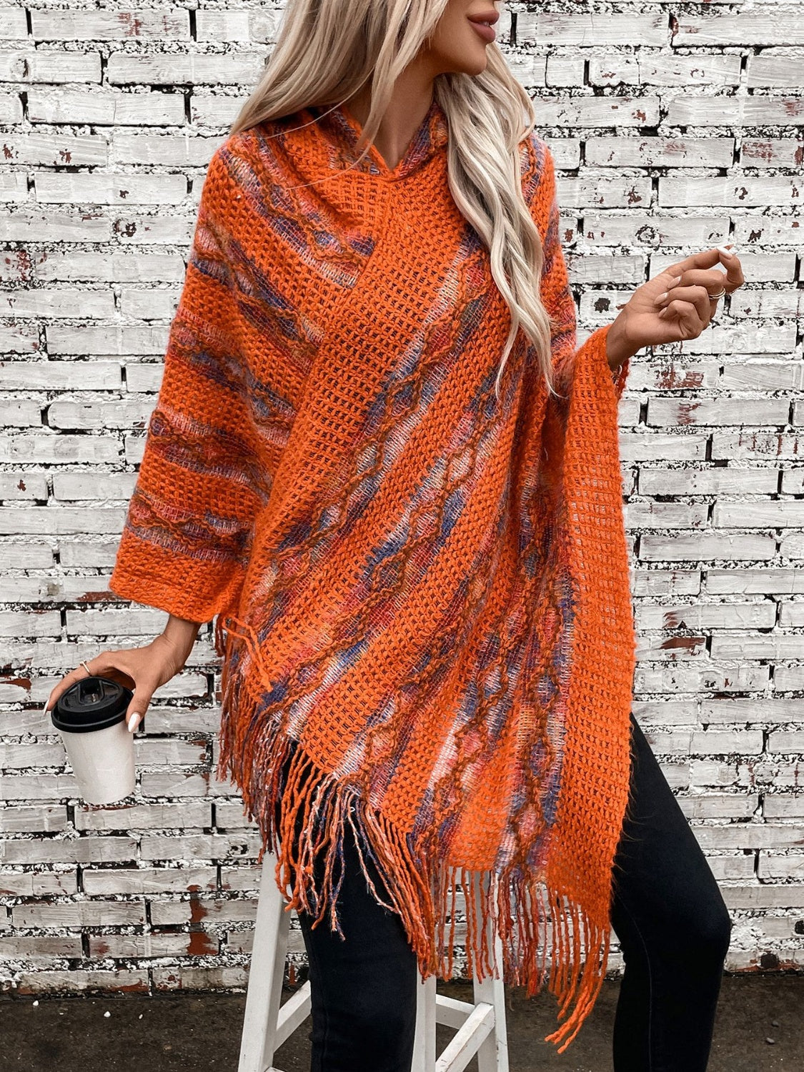Textured knit hooded fringed cape in terracotta with colorful accents and fringe detail.