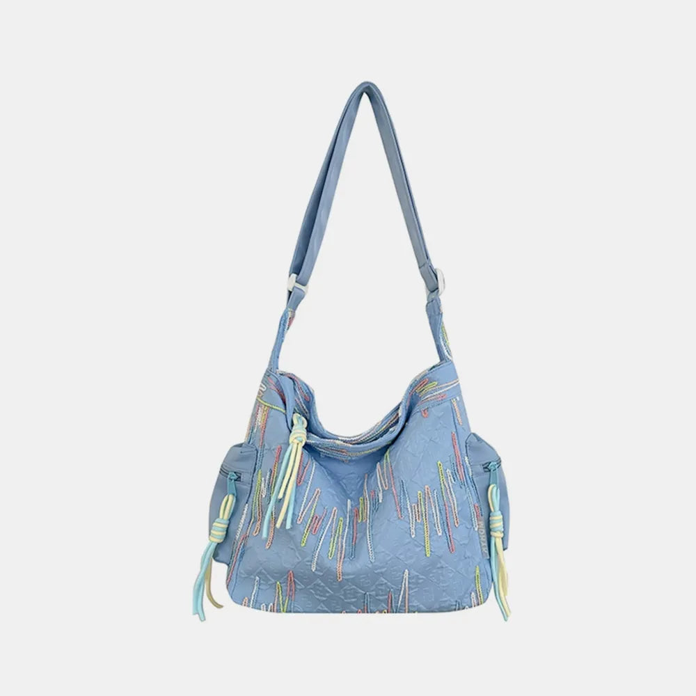Light blue slouchy shoulder bag with colorful embroidered lines and tassels