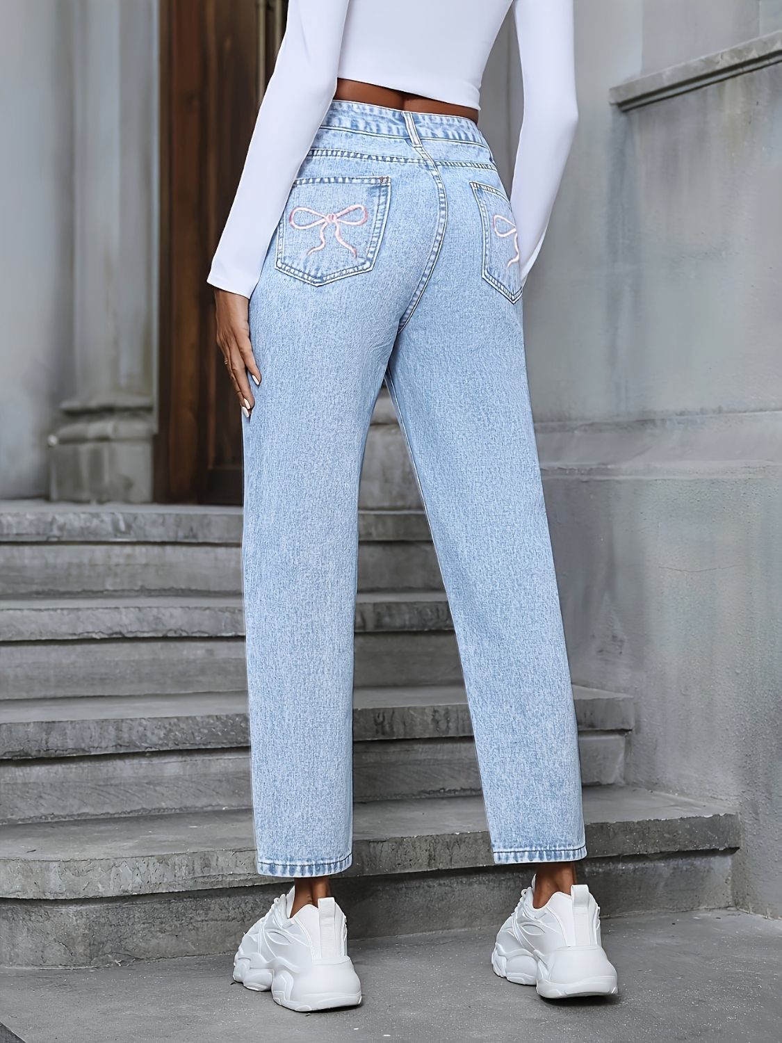 Light wash boyfriend jeans with distressed details and pink bow embroidery on back pockets.