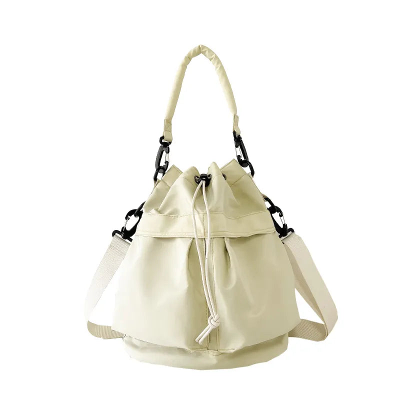 Drawstring nylon bucket bag in beige with chain detail and adjustable strap.