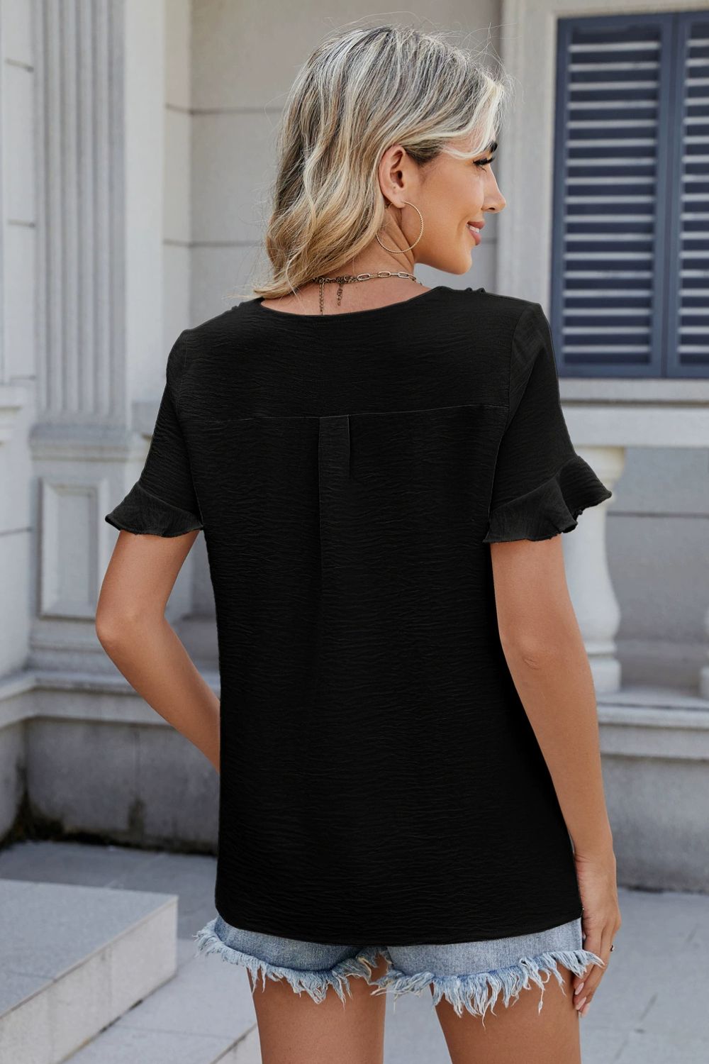 Black textured pleat front blouse with flutter sleeves and a button back detail.