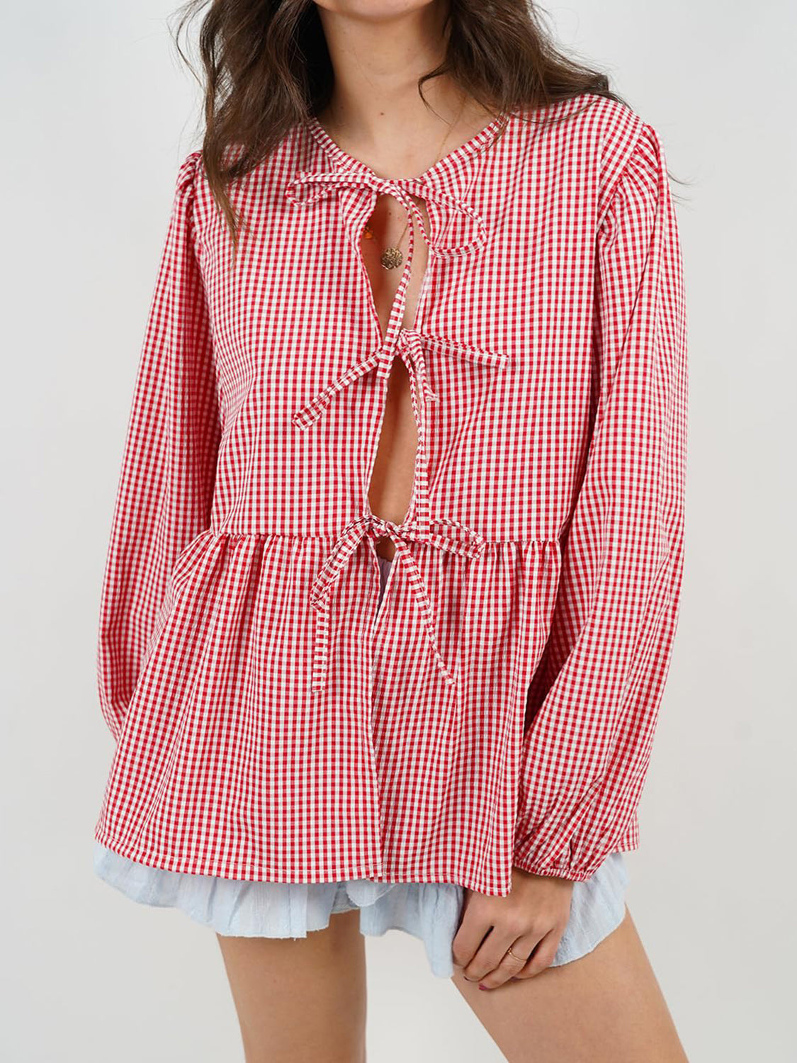 Red gingham tie-front peplum blouse with voluminous sleeves and a ruffled hem.