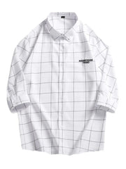 White oversized button-down shirt with black plaid print and embroidered text detail.