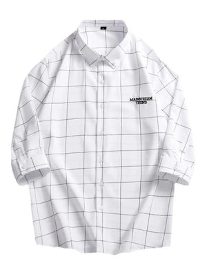 White oversized button-down shirt with black plaid print and embroidered text detail.