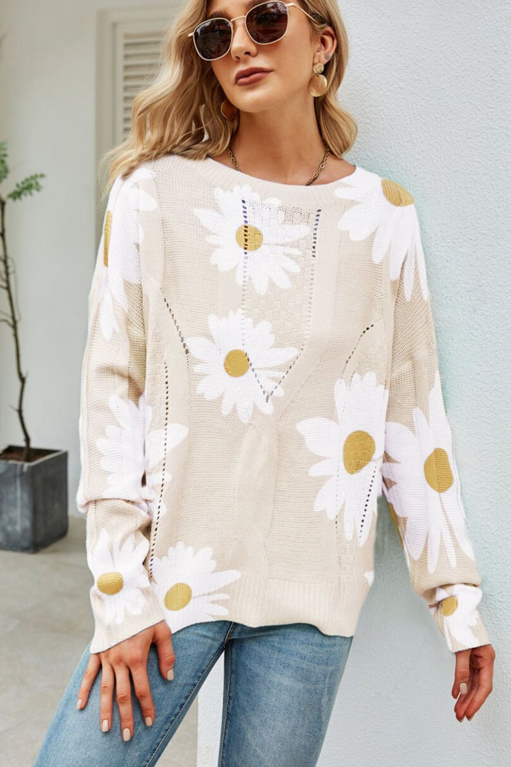 Beige intarsia knit sweater with white daisies, long sleeves, and open knit details.
