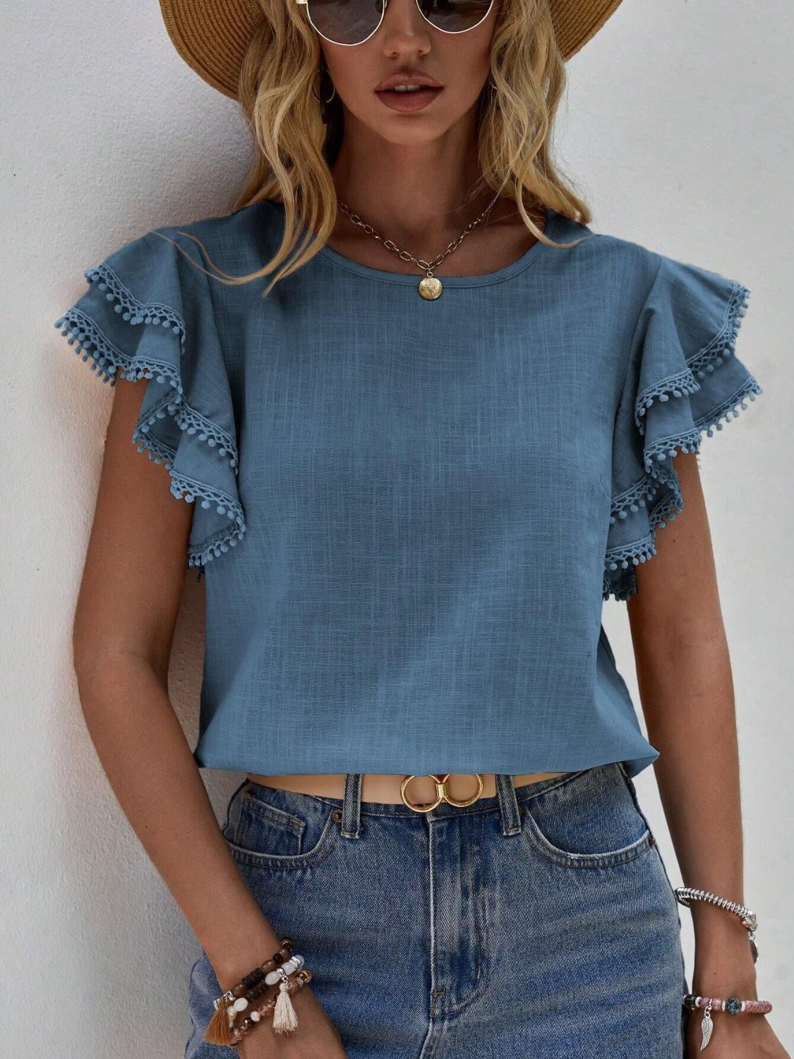 Dusty Blue ruffle sleeve blouse with pom-pom trim and round neckline.