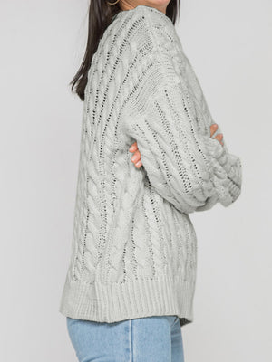 Grey cable knit openwork sweater with crew neck and long sleeves.