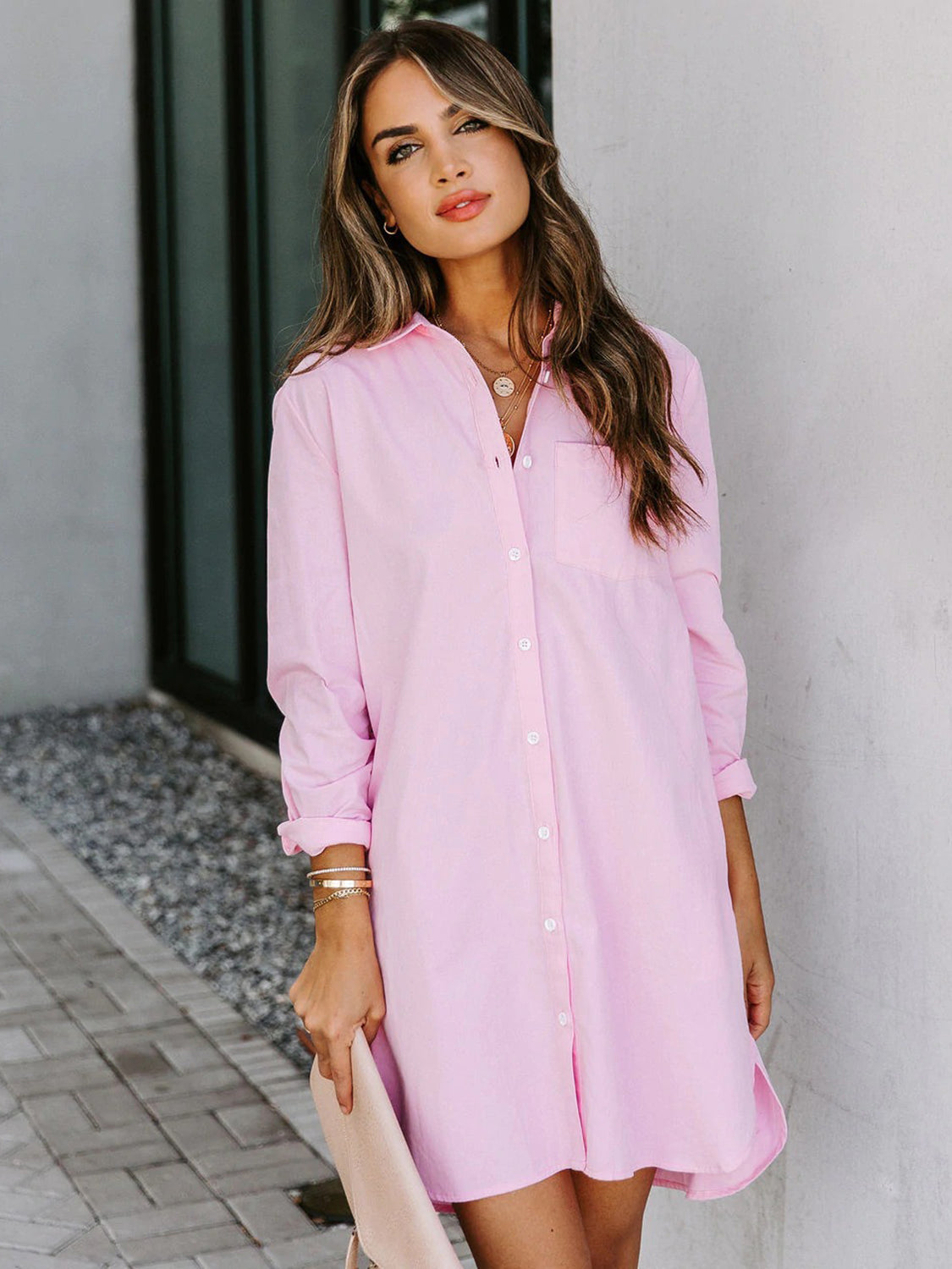 Oversized pink cotton shirt dress with button front and curved hem.