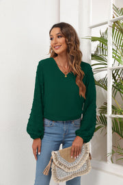 Forest green V-neck blouse with textured pom-pom sleeves and balloon cuffs.