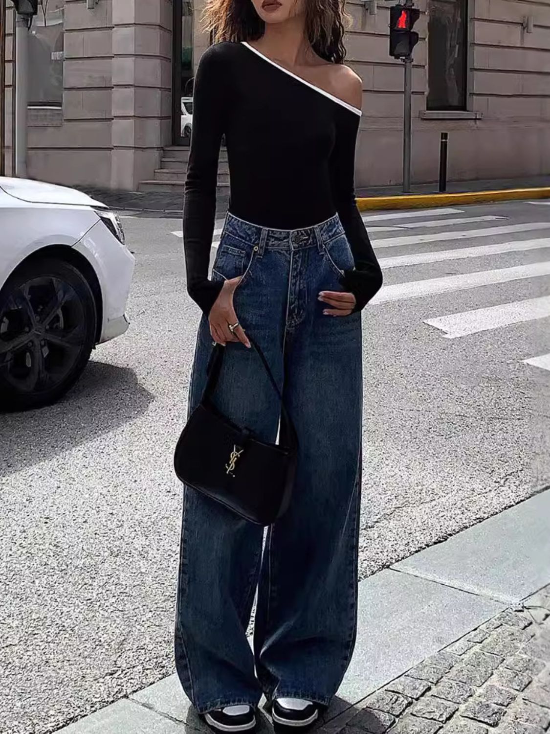 Black off-shoulder ribbed top with contrast trim, long sleeves, paired with wide-leg jeans.