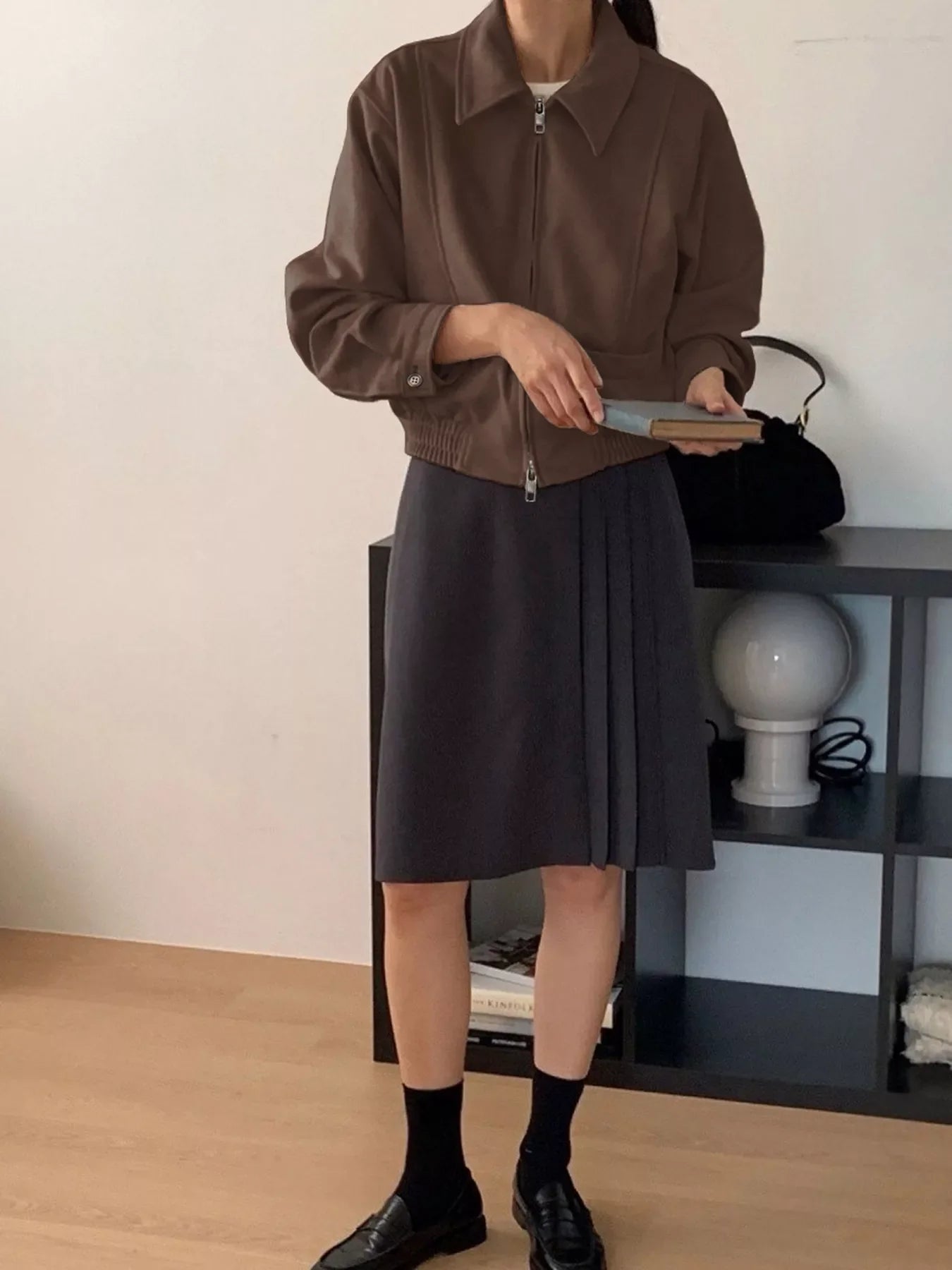 Brown zip up long-sleeve jacket with collar and elastic hem, styled with a dark skirt.