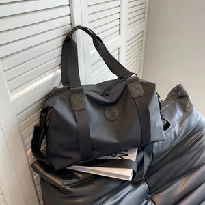 Black canvas duffel bag with adjustable strap and embossed logo detail.