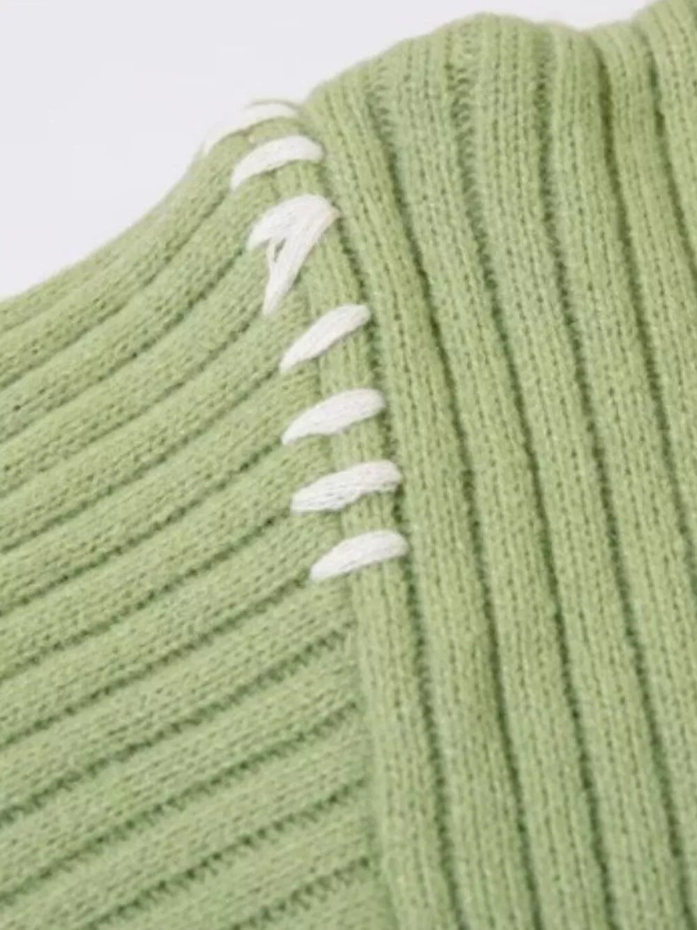 Green ribbed knit sweater with abstract white contrast stitching detail on shoulder.