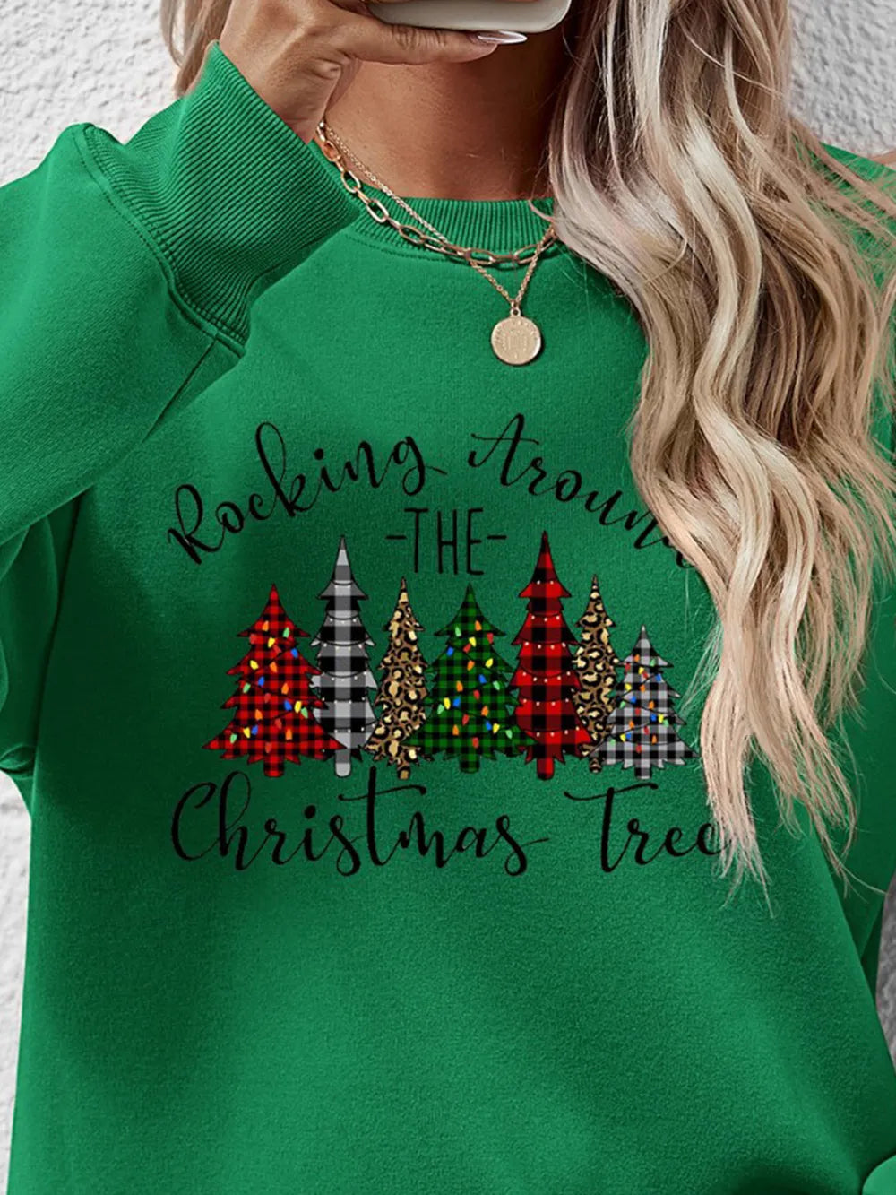 Green crewneck sweatshirt with graphic Christmas trees and "Rocking Around The Christmas Tree" text.