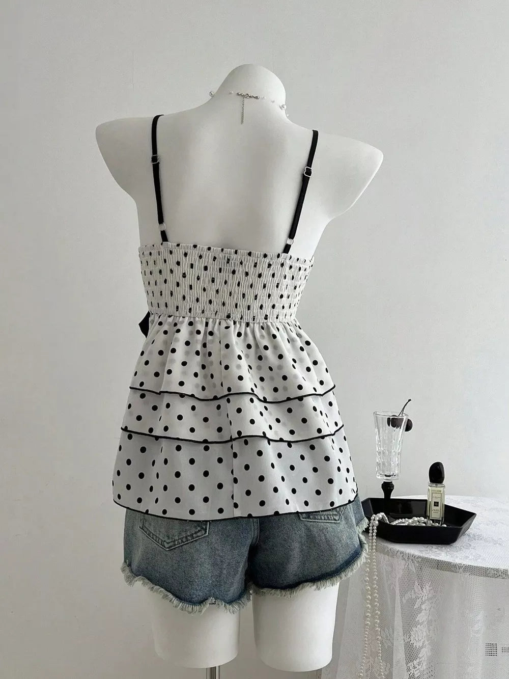 White polka dot camisole with black trim, smocked bodice, tiered ruffle hem, and adjustable straps.