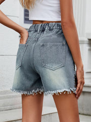 Medium wash denim shorts with frayed hem and studded side detail