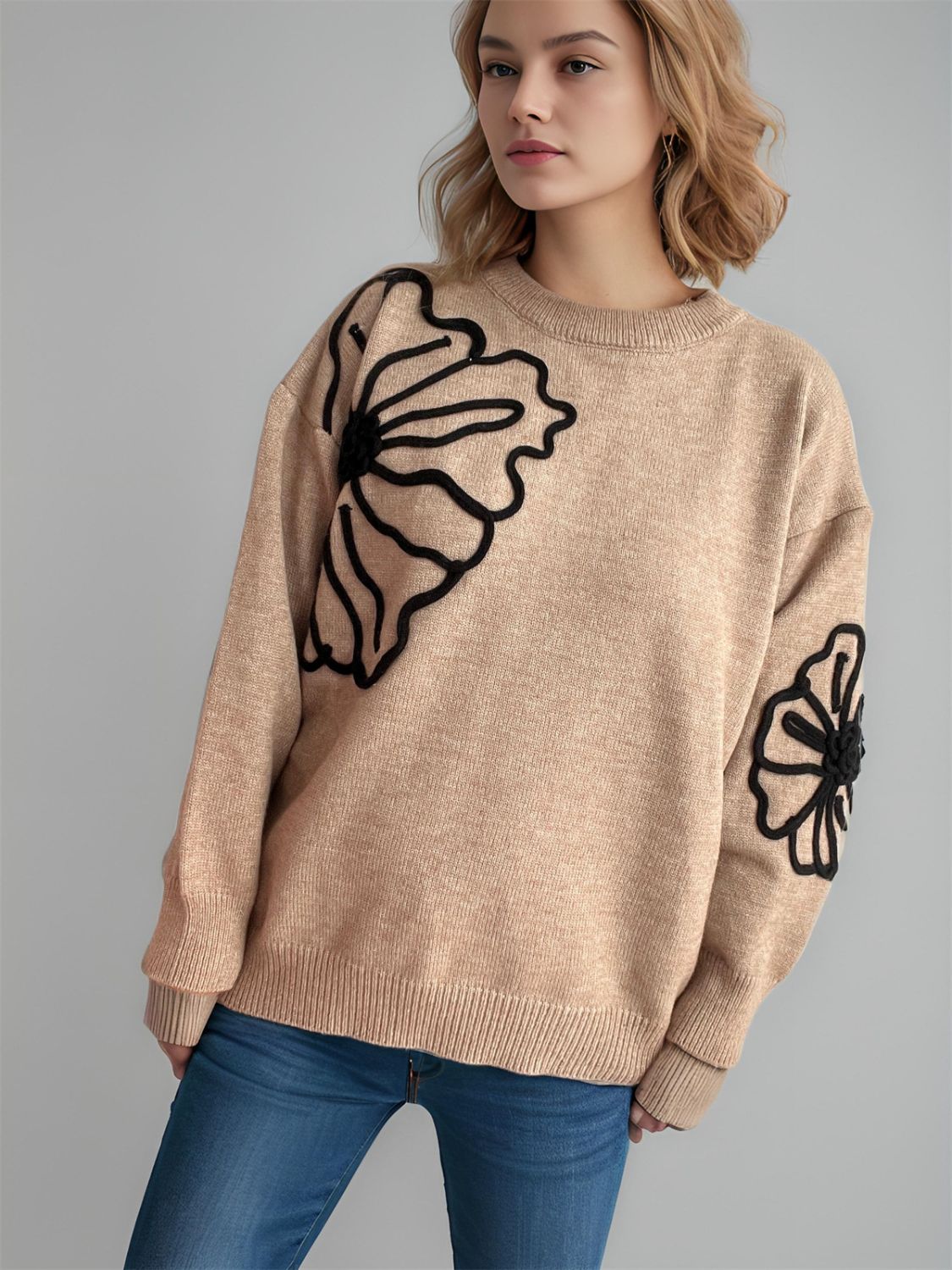 Tan crewneck sweater with black floral embroidery on the chest and sleeve.