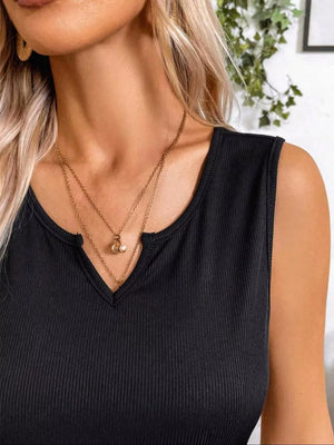 Black ribbed knit tank dress with notch neckline and layered necklaces.