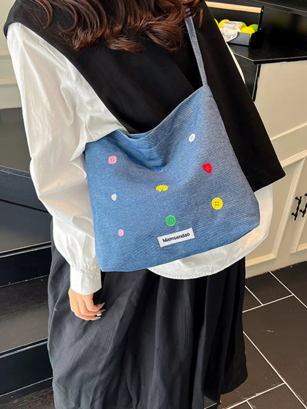 Light blue denim crossbody bag with colorful embroidered buttons and adjustable strap.