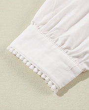 White linen blouse with scalloped pom-pom trim and gathered sleeve detail.