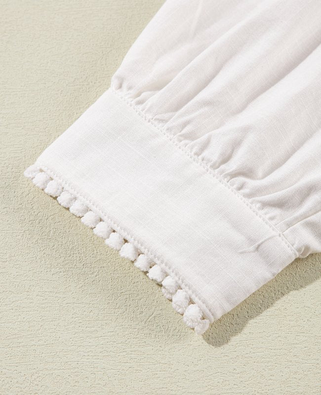 White linen blouse with scalloped pom-pom trim and gathered sleeve detail.