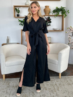 Black wrap jumpsuit with V-neck, short sleeves, tie waist, and high slit legs.