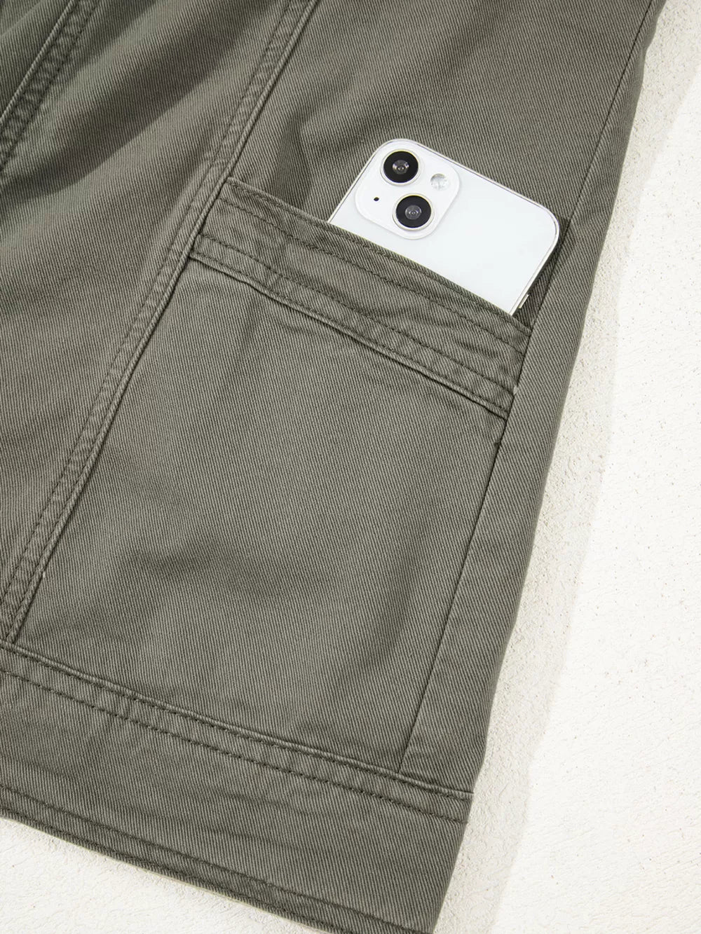 Ruffled denim vest in olive green cotton with a button closure and a phone in the pocket.