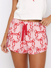 Blush pink lounge shorts with red bow print and red drawstring.