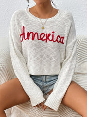 Ivory knit sweater with red embroidered "America" text, crew neck, long sleeves.