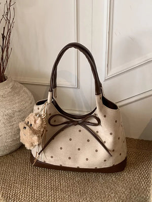 Tan polka dot shoulder bag with brown trim, bow detail, and fuzzy charm.
