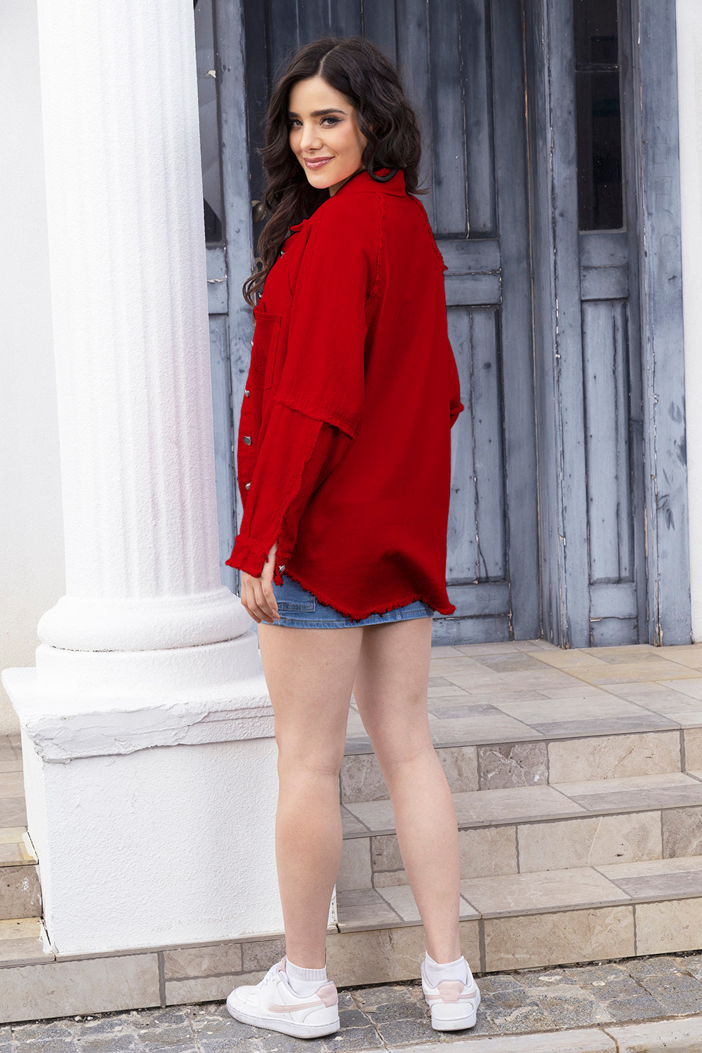 Red denim jacket with raw edges and button-down front, styled with denim shorts.
