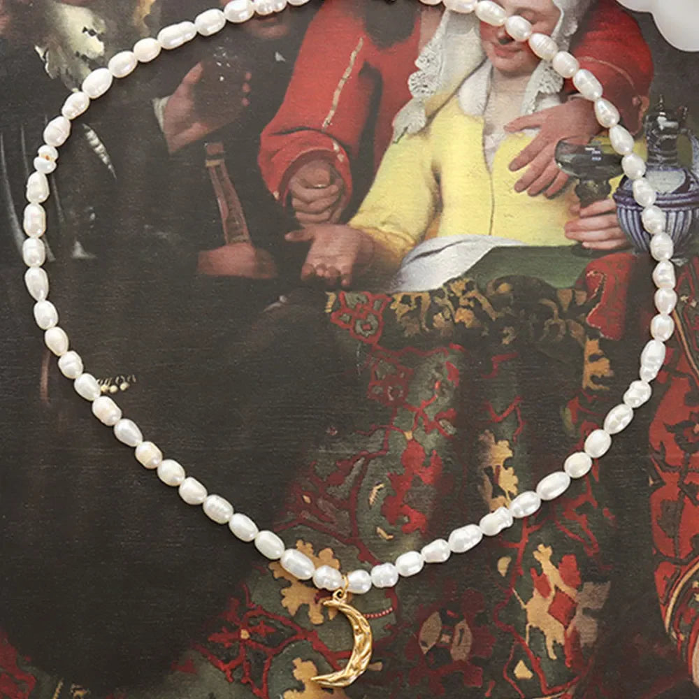 Gold crescent moon necklace with a delicate pearl strand.
