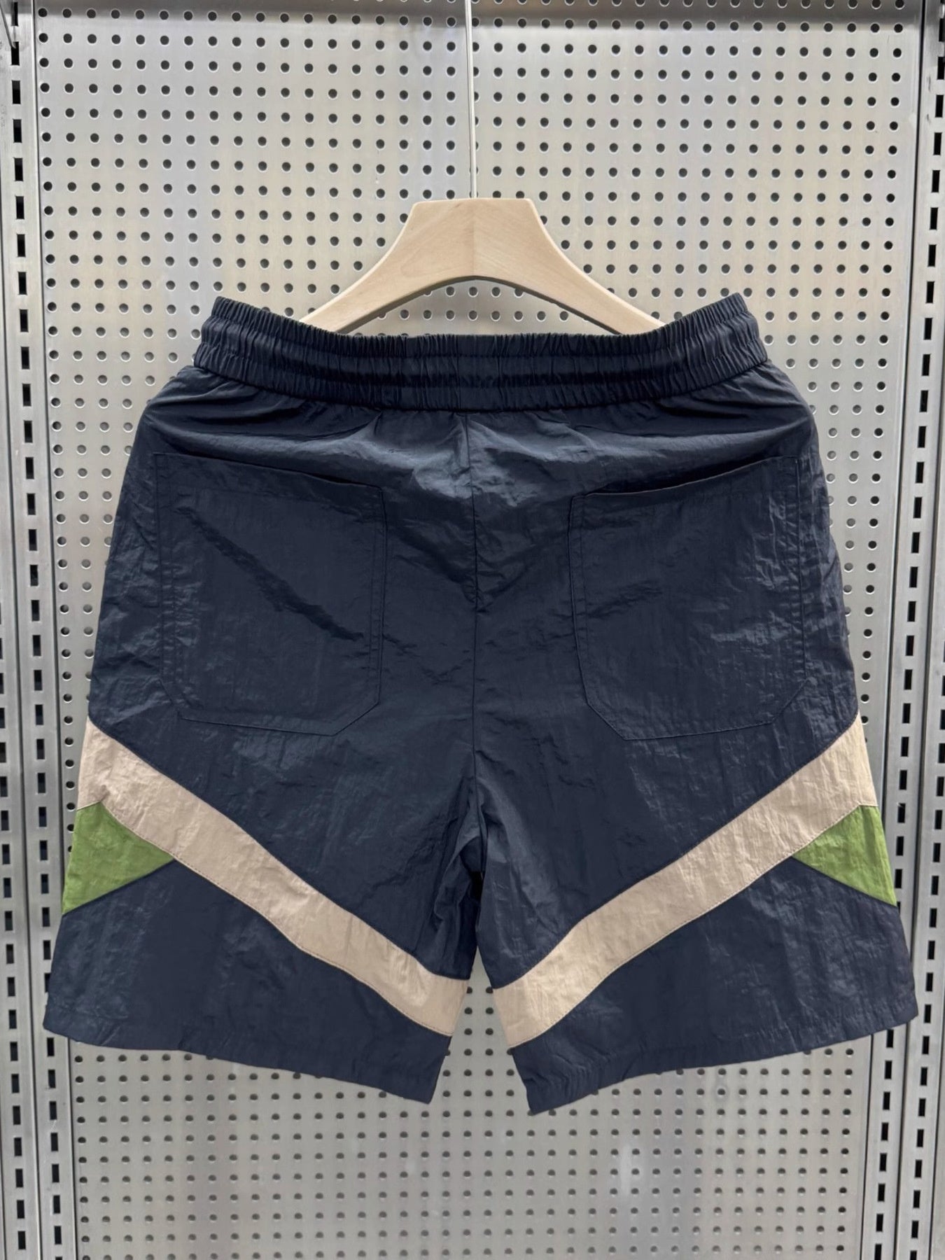 Men's shorts in dark blue with beige and green color block accents and elastic waistband.