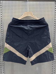 Men's shorts in dark blue with beige and green color block accents and elastic waistband.