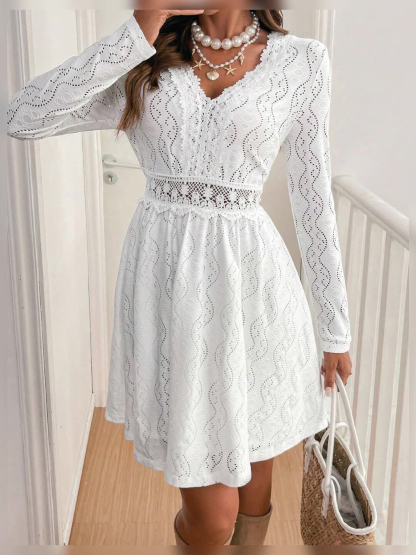 White lace a-line dress with V-neck, long sleeves, and openwork details.