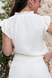 White textured eyelet trim tie-neck blouse with ruffled neckline and cap sleeves.