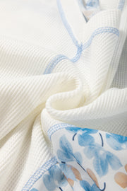 White waffle knit blouse with blue floral print sleeves and contrast stitching.