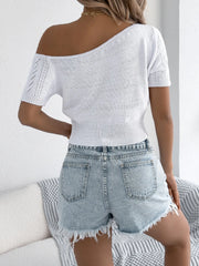 White open-knit crop top with asymmetric neckline and short sleeves, styled with denim shorts.