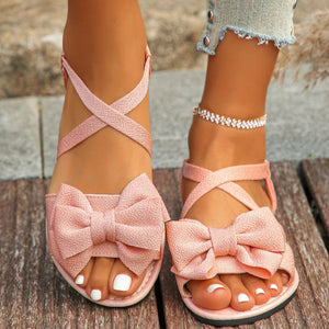 Pink crisscross bow sandals with ankle straps and open toe.