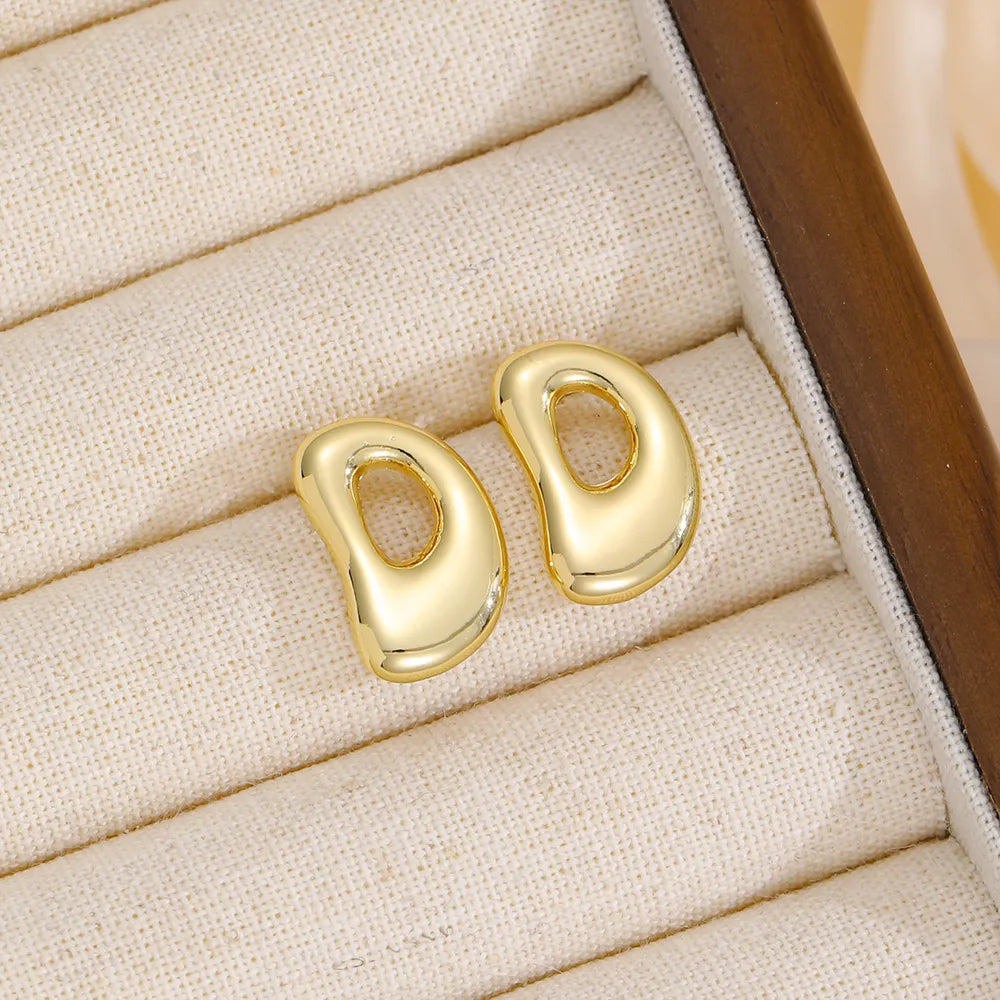 Gold sculptural stud earrings in the shape of the letter D.