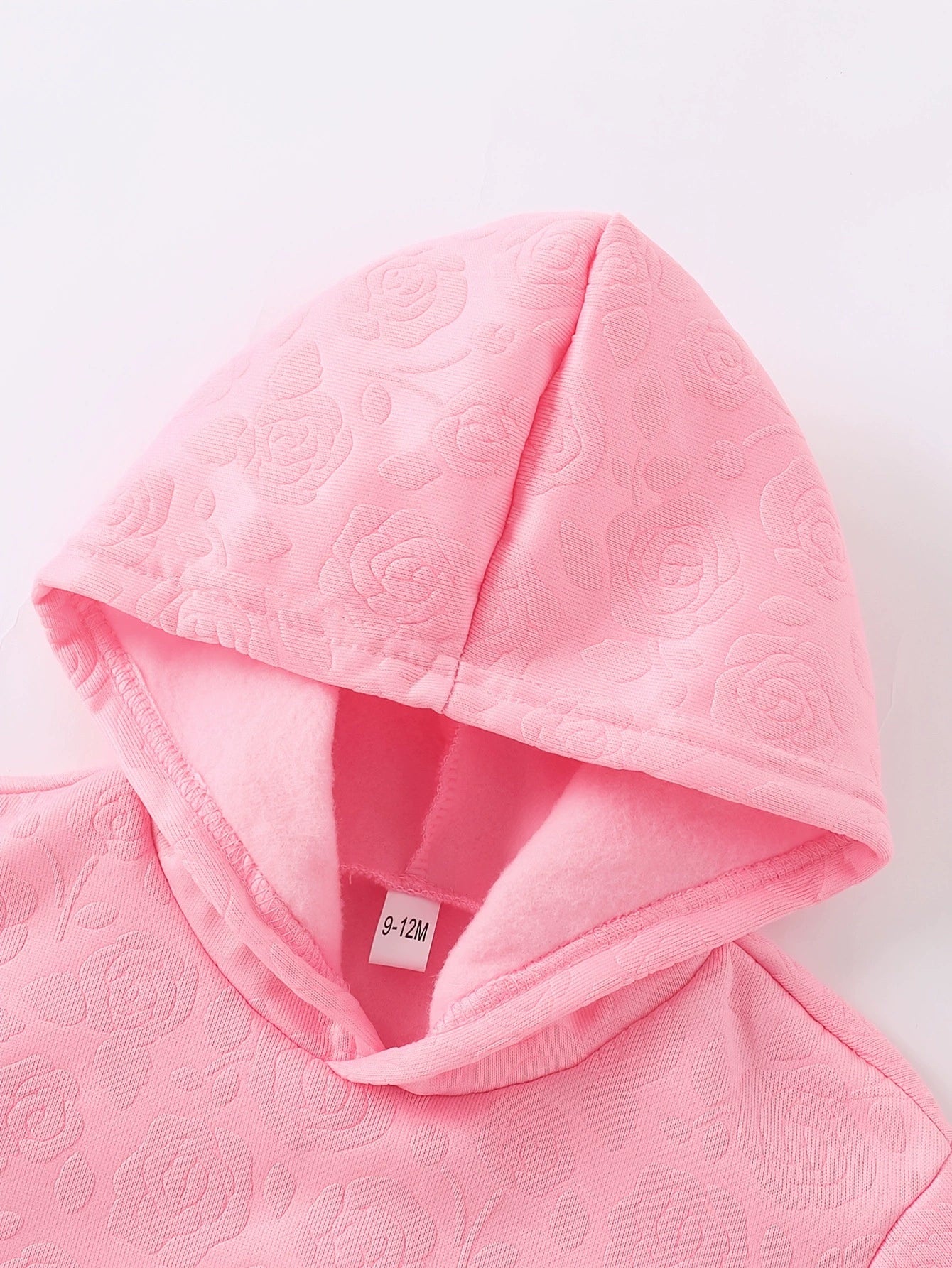 Pink embossed floral baby hoodie with soft lining and size tag.